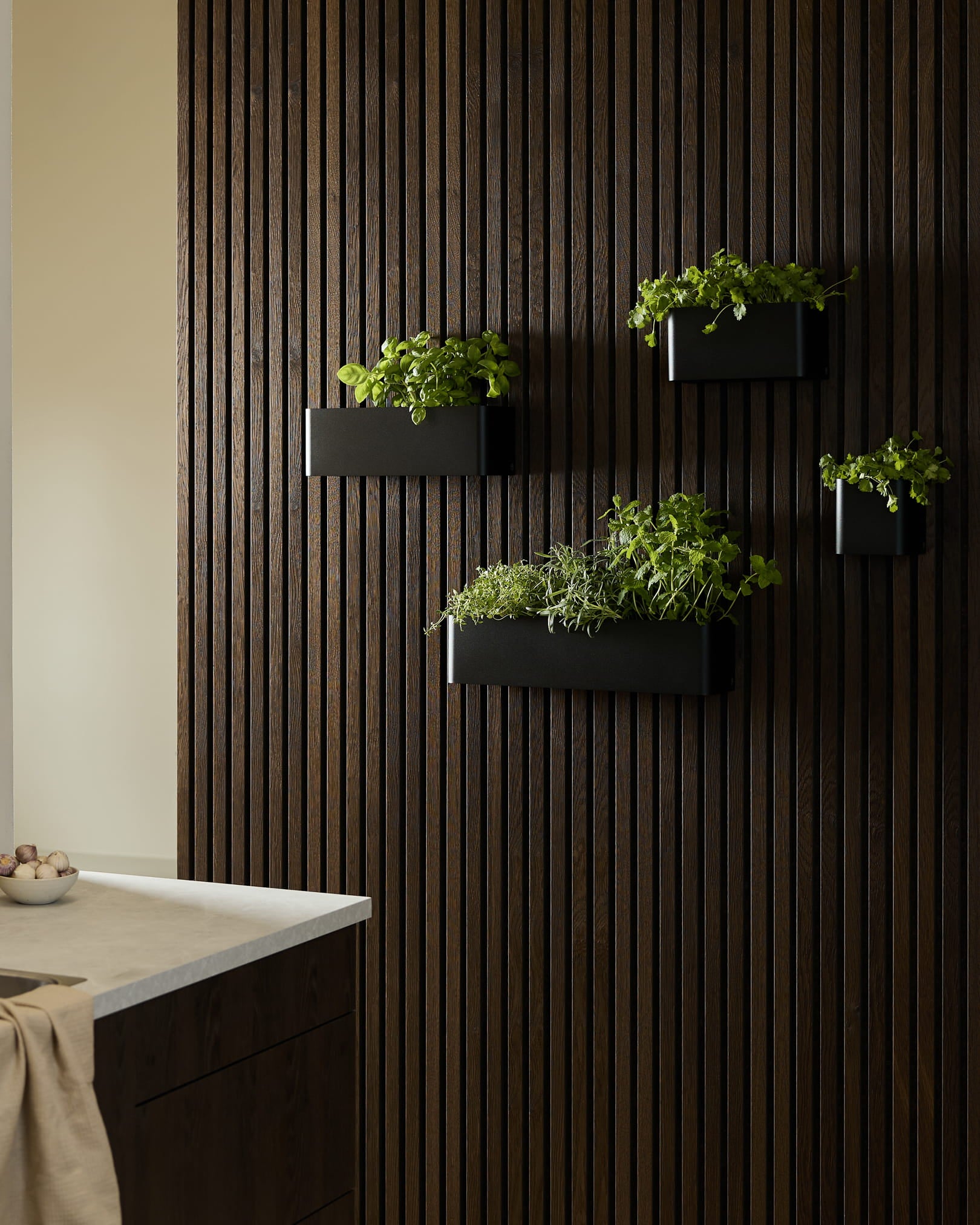 Black väggmonterade planteringslådor och en WoodUpp Norr Plant Box med gröna örter på en mörk träfärgad Akupanel Akustikpanel i ett modernt kök.
